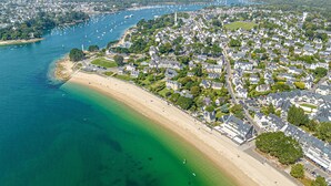 An aerial view of a coastal town with a beach, residential areas, and a marina.