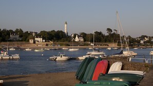 A harbor with boats, a lighthouse, and houses in the background.