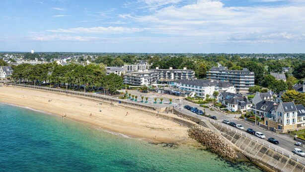 Een hotel aan de kust met meerdere gebouwen, een zandstrand en een helderblauwe lucht.