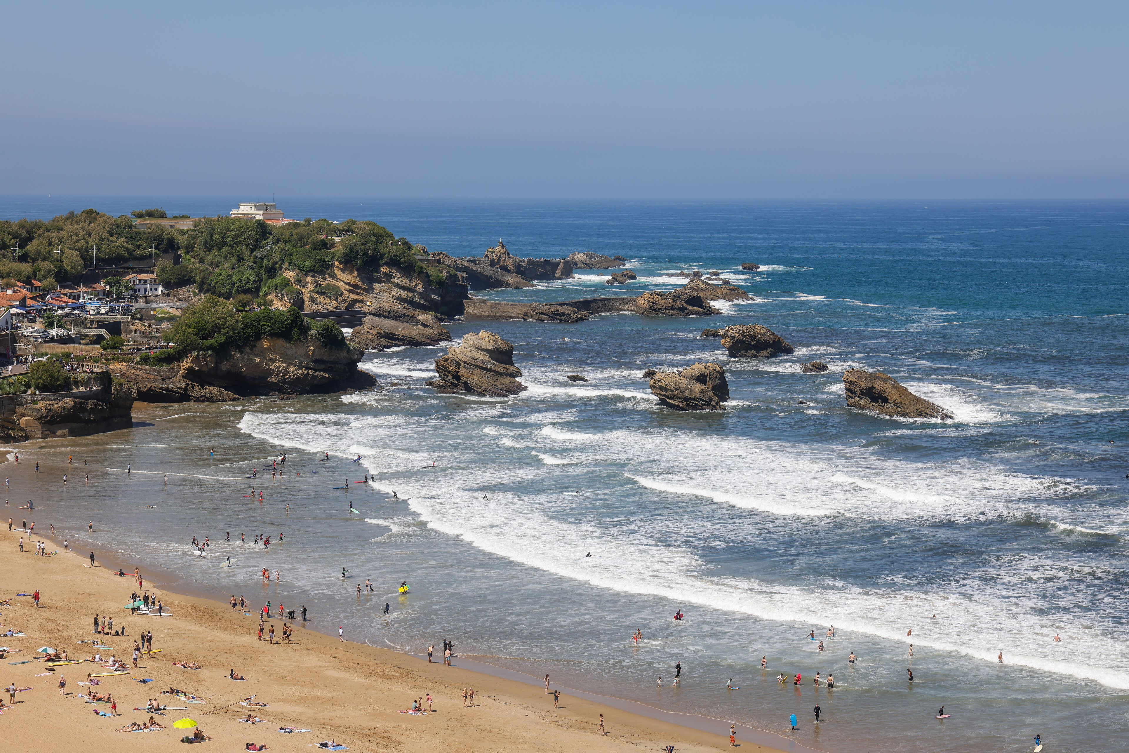A beach with rocky outcrops, waves, and people enjoying the shore.