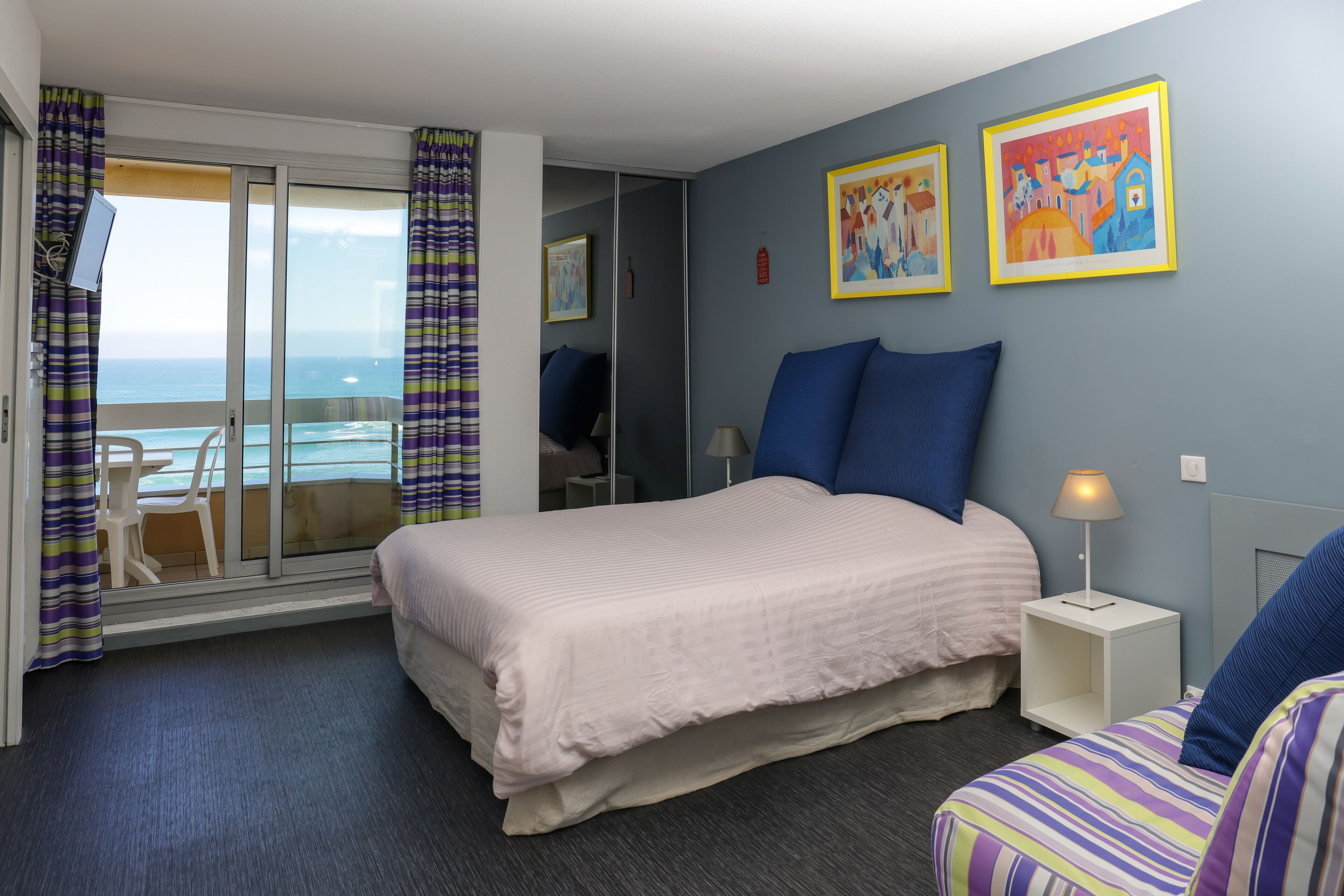 A hotel room with a bed, a chair, a desk, and a view of the ocean.