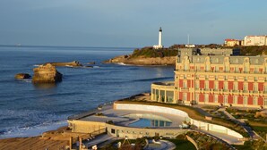 A coastal hotel with a pool, a lighthouse, and rocky cliffs. - Résidence Victoria Surf (Biarritz)