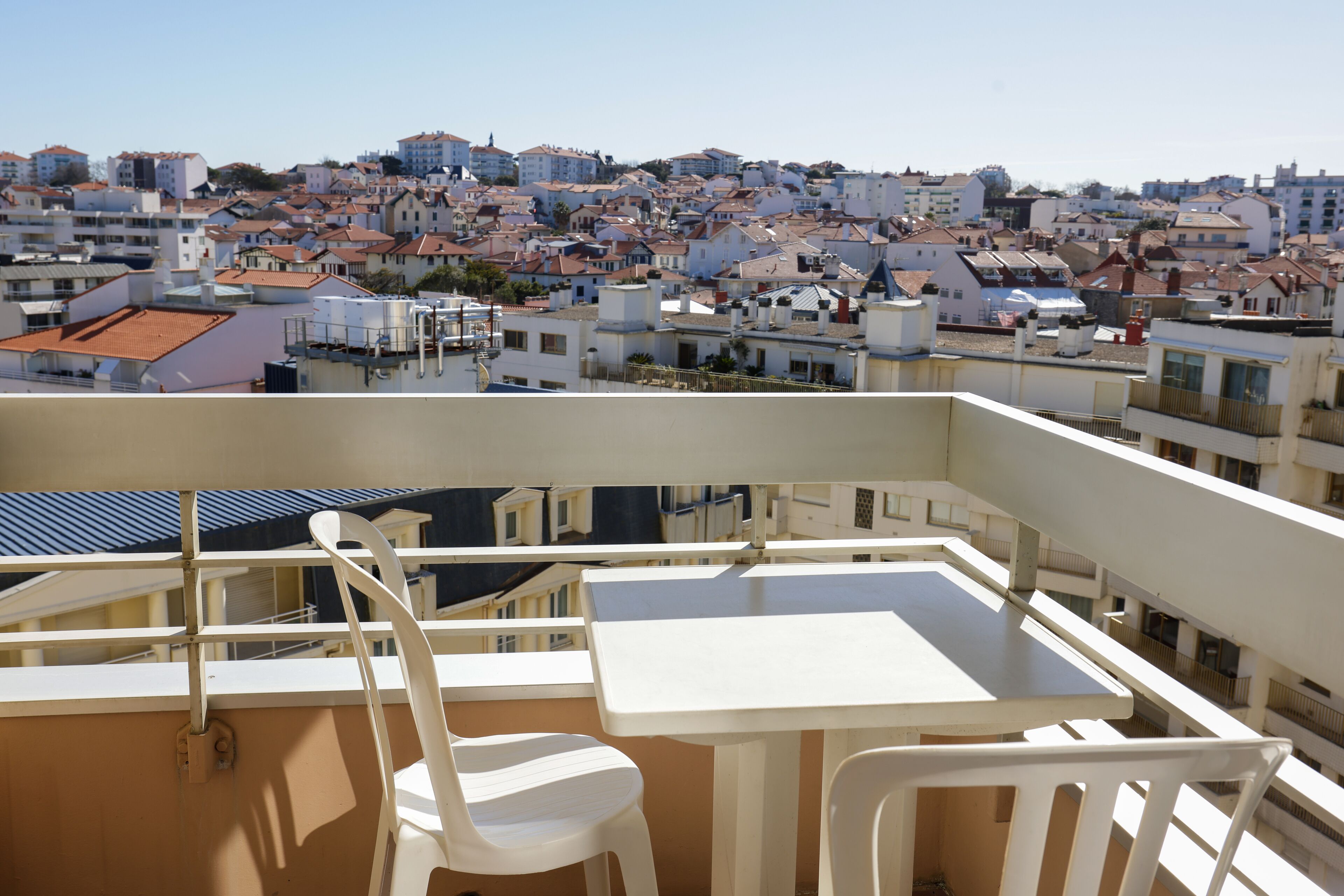 Un balcon avec une table et des chaises, donnant sur un quartier résidentiel densément peuplé, composé de différents types d’immeubles.