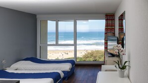 A bedroom with two beds, a desk, and a view of the beach and ocean. - Résidence Victoria Surf (Biarritz)