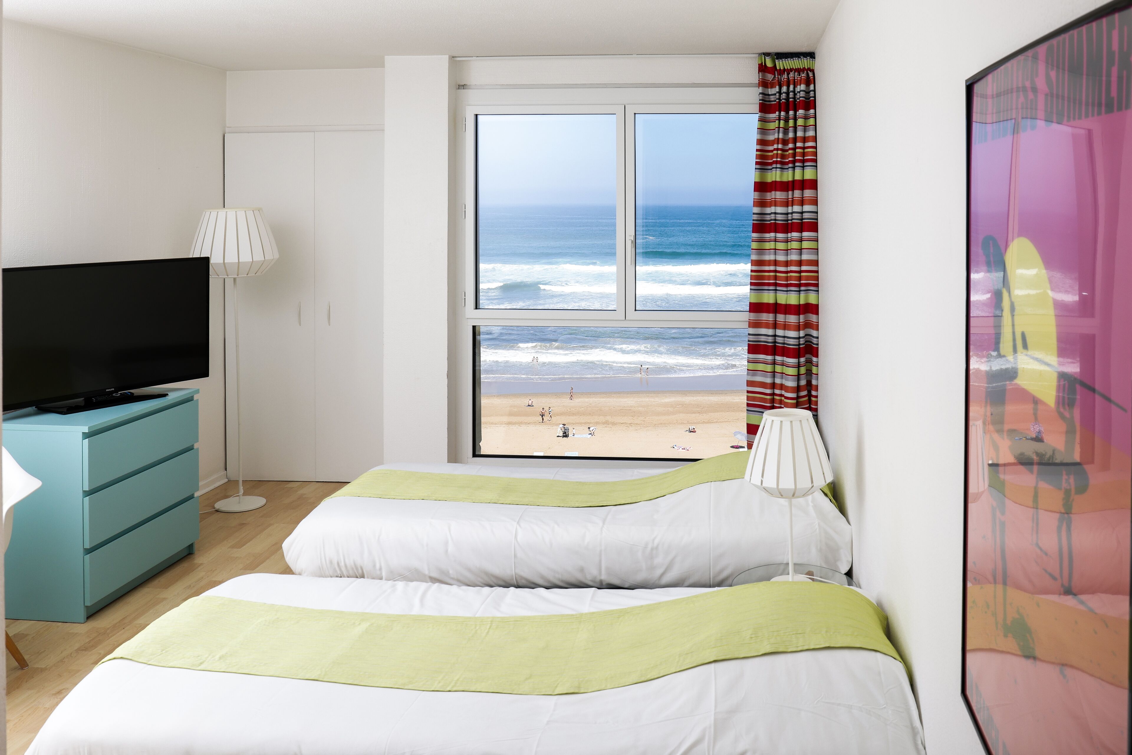 Une chambre d’hôtel avec un lit, une télévision, une commode et une fenêtre donnant sur la plage.