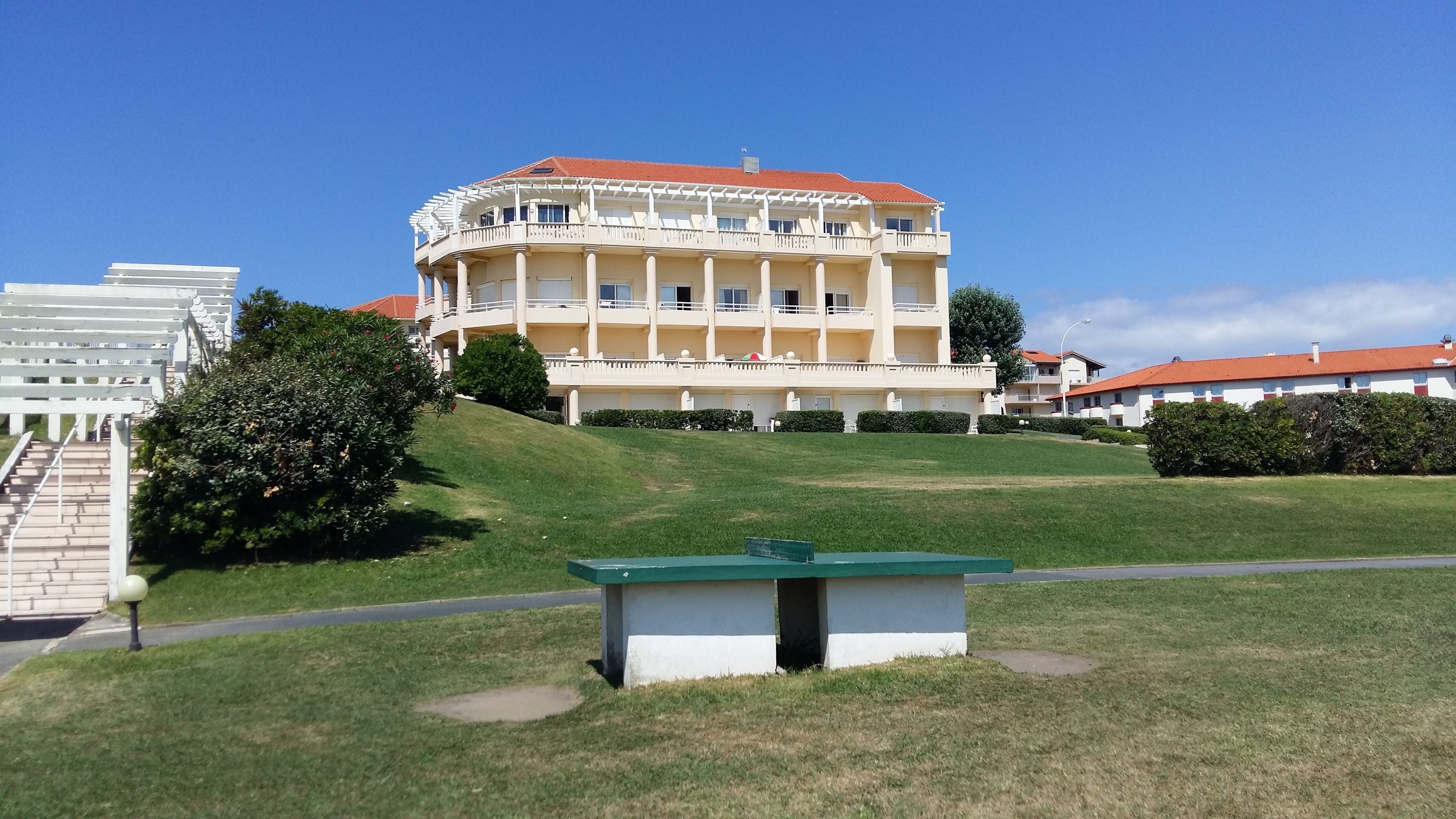 A multi-story hotel with a red roof, white balconies, and a well-maintained lawn.