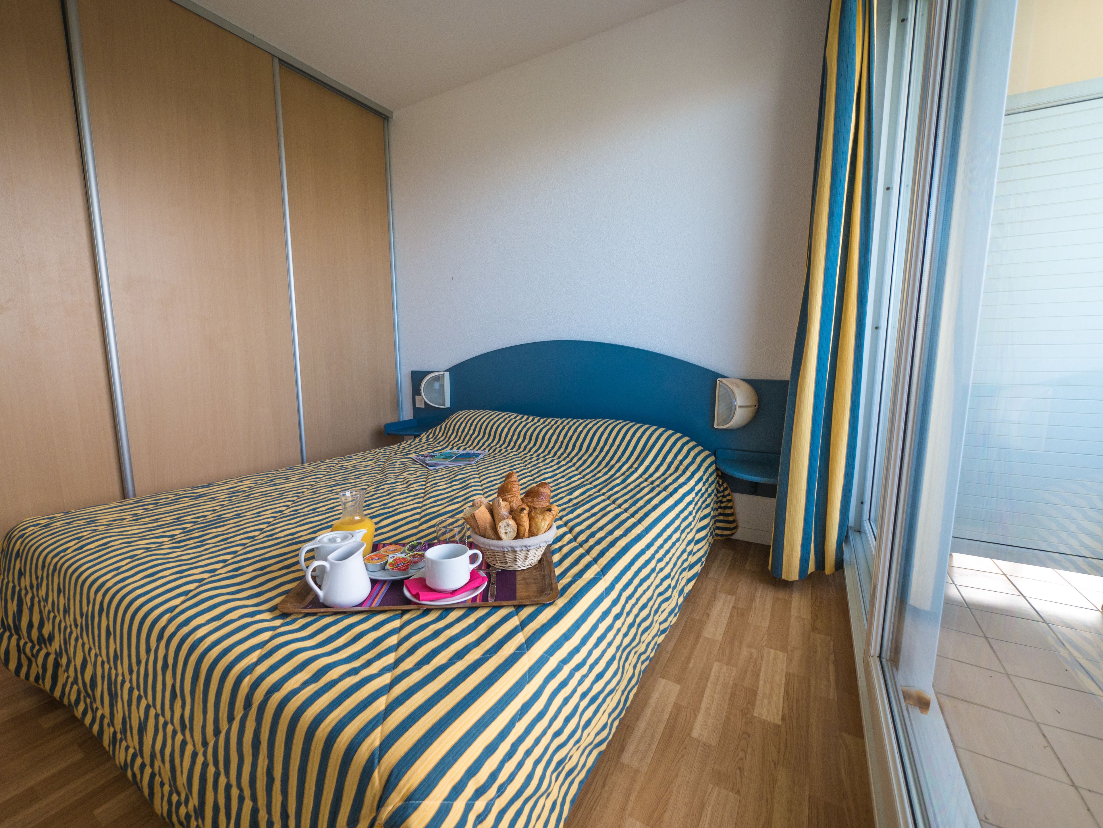 Habitación de hotel con cama, mesita de noche, ventana con cortinas y vistas al exterior.