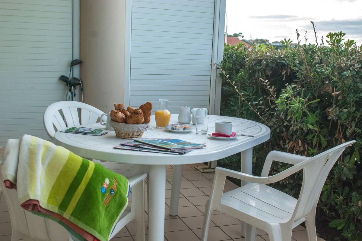 A round table with chairs, a basket of bread, a glass of orange juice, and a magazine.
