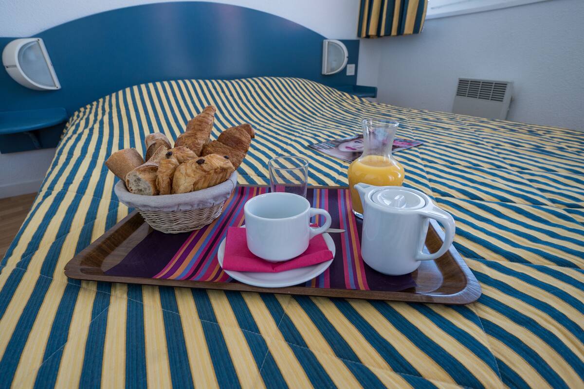 A breakfast tray with croissants, a glass of orange juice, and a white mug on a striped bedspread.