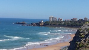 A coastal beach with rocky outcrops, a sandy shore, and buildings in the background. - Résidence Eugénie (Biarritz)