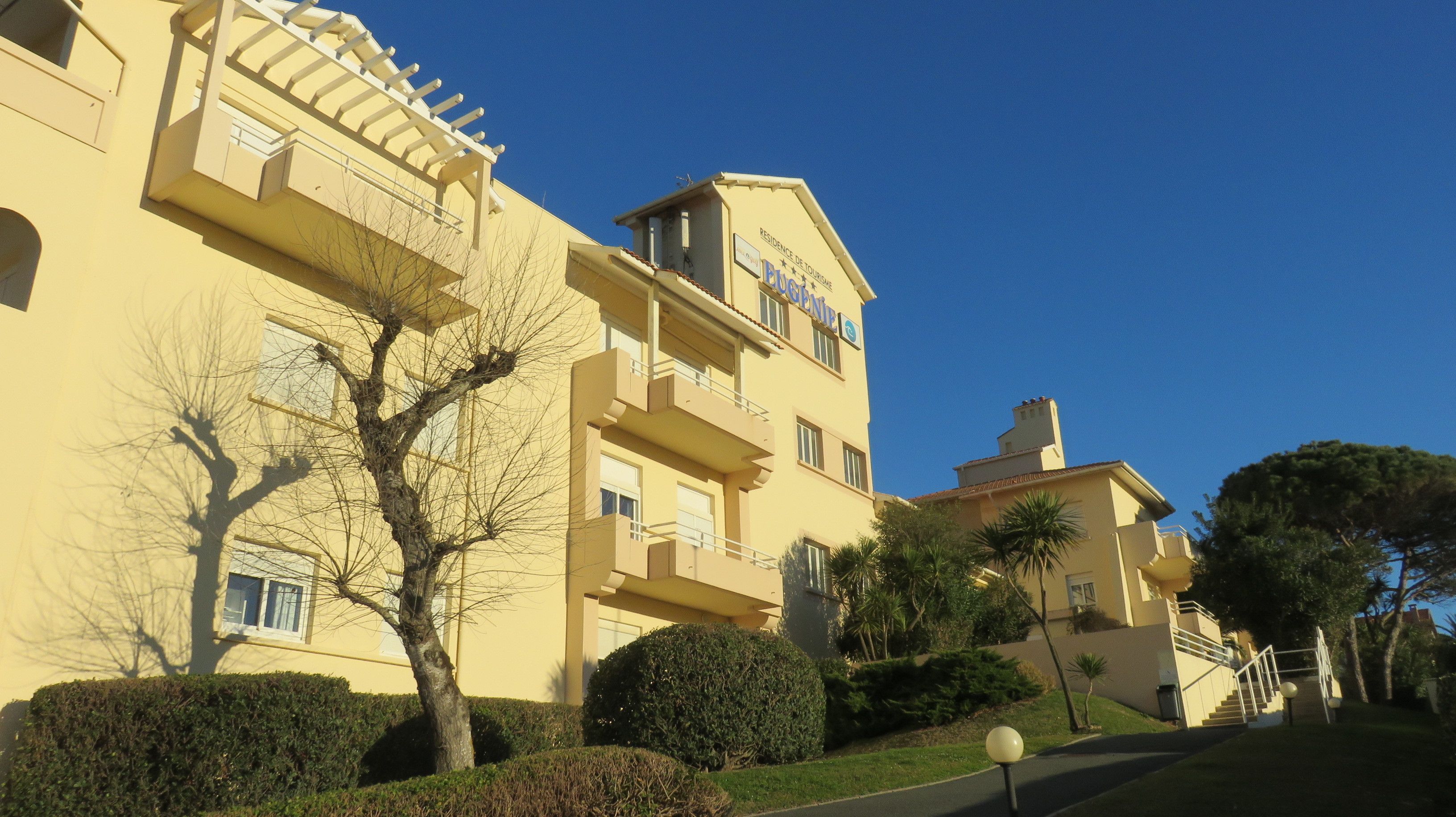 A multi-story hotel with balconies, a clear blue sky, and well-maintained landscaping.