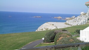 A coastal view with a clear sky, rocky terrain, and a paved path leading to a grassy area. - Résidence Eugénie (Biarritz)