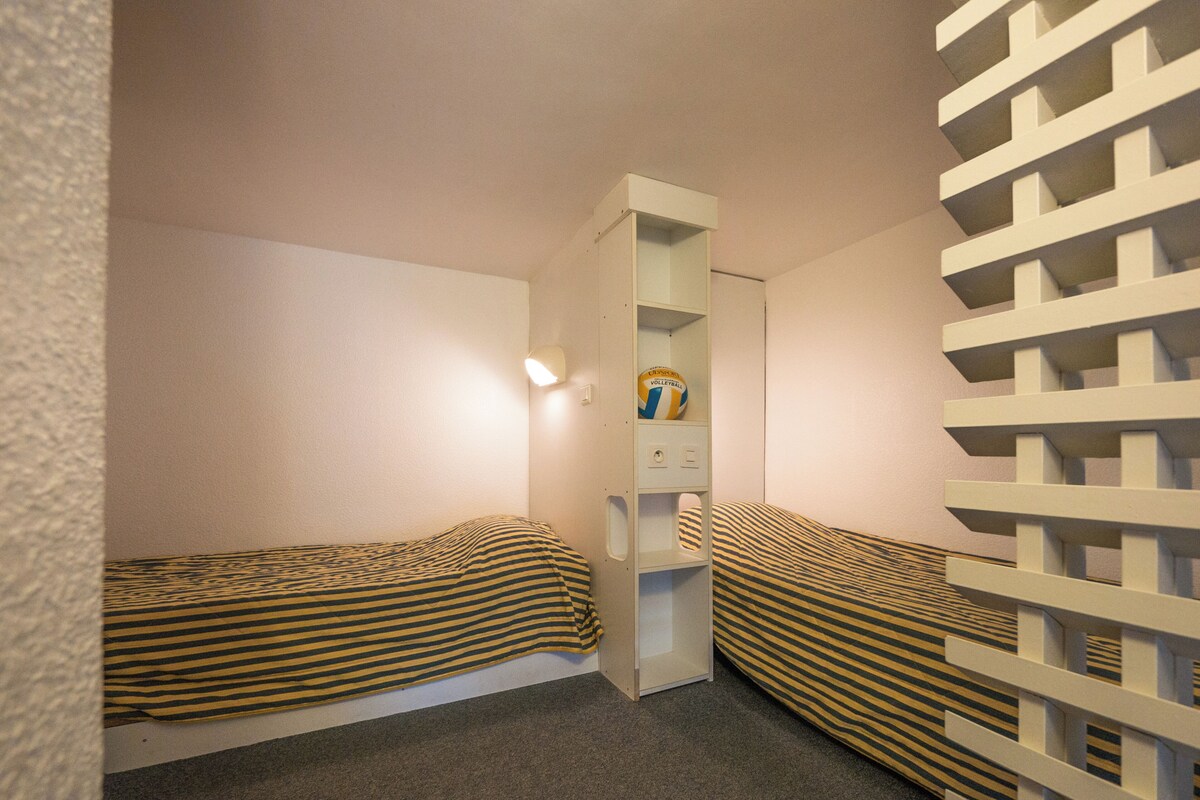 A small room with two beds, a shelf with a volleyball, and a white partition.