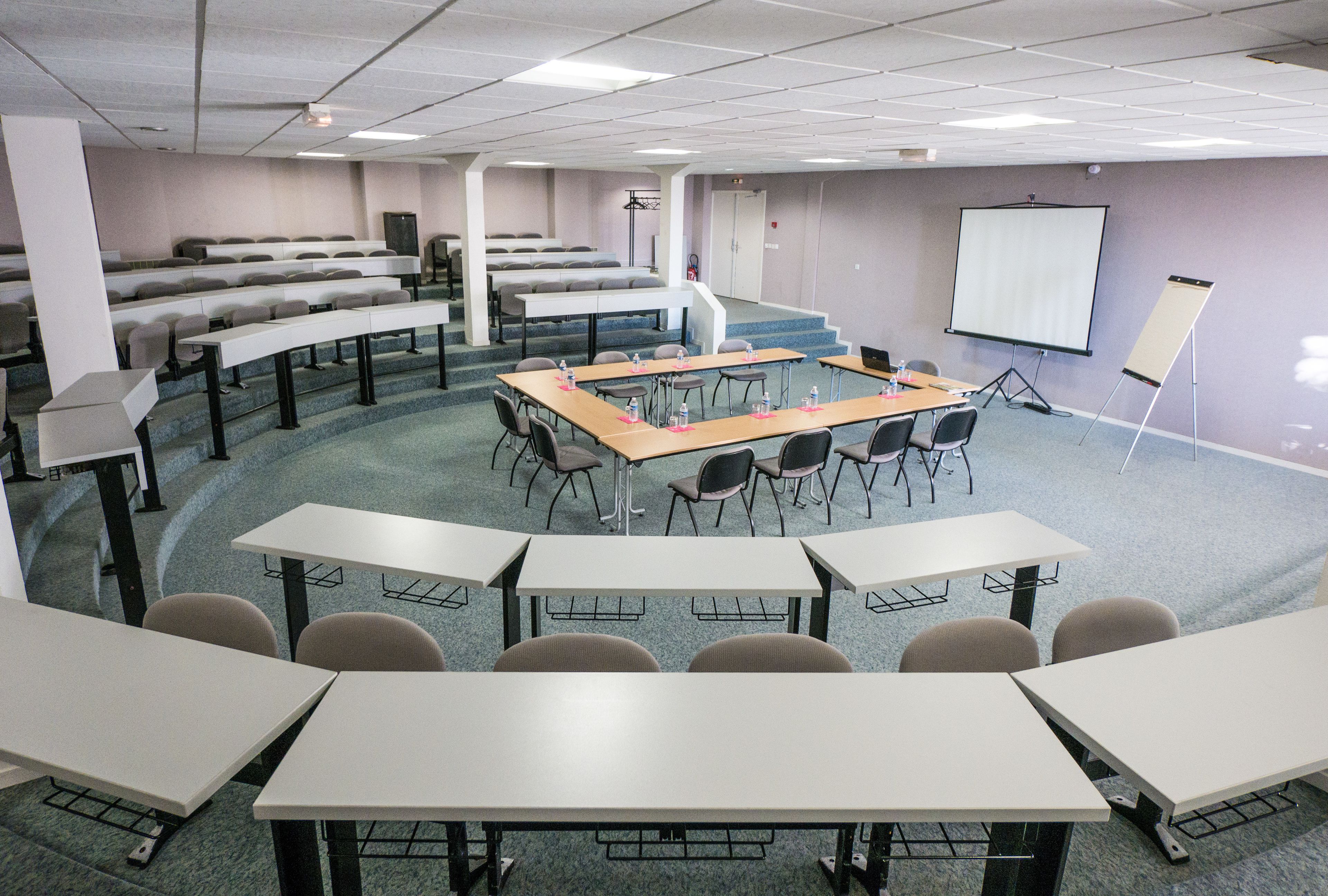 A conference room with tiered seating, a central table, and a projection screen.