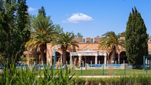 Un edificio con entrada central que dice "FORUM", rodeado de palmeras y un cuerpo de agua.
