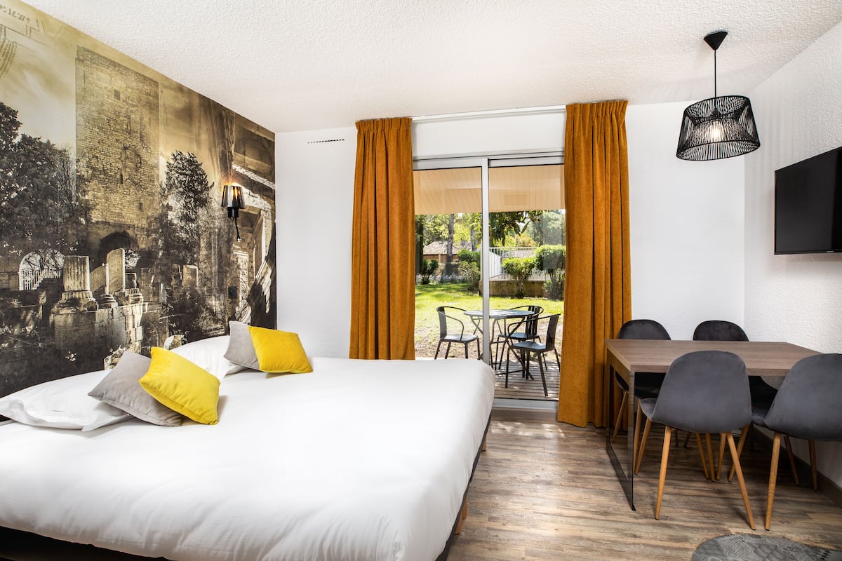 A hotel room with a large bed, a dining table with chairs, a TV, and a mural on the wall.