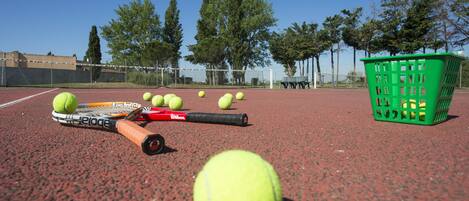 Un court de tennis avec un panier de balles de tennis, une raquette de tennis et un banc.