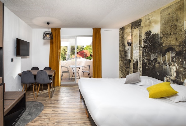 Une chambre d’hôtel avec un lit, un bureau avec des chaises, une télévision et une fresque murale.