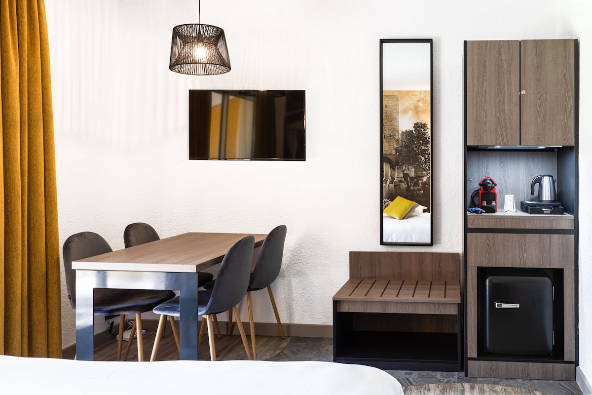 A modern hotel room with a wooden dining table, black chairs, a black refrigerator, and a small kitchenette.
