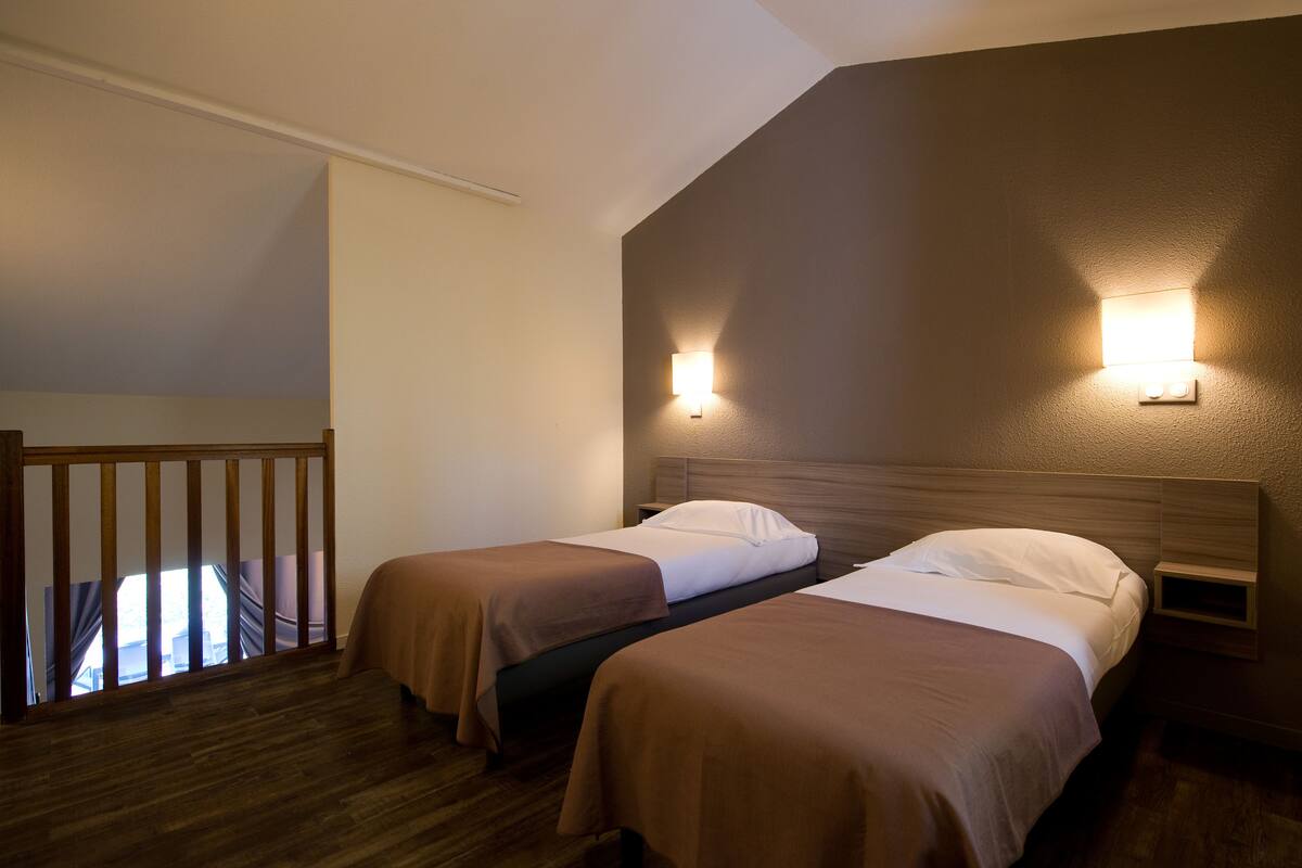 Ein Hotelzimmer mit zwei Betten, Holz-Kopfteilen, einem kleinen Nachttisch und einer Wandleuchte.