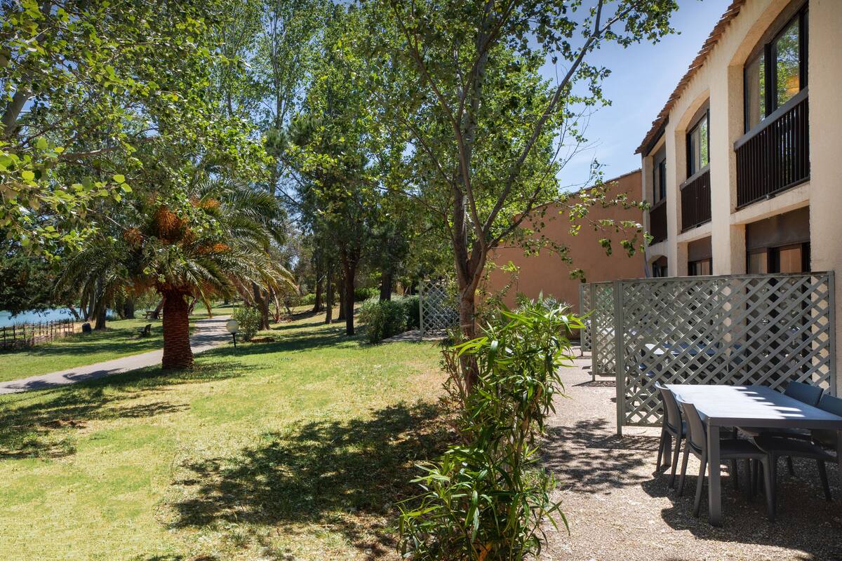 Eine Terrassenanlage mit Tisch und Stühlen, umgeben von Bäumen und einem Gebäude mit Balkonen.