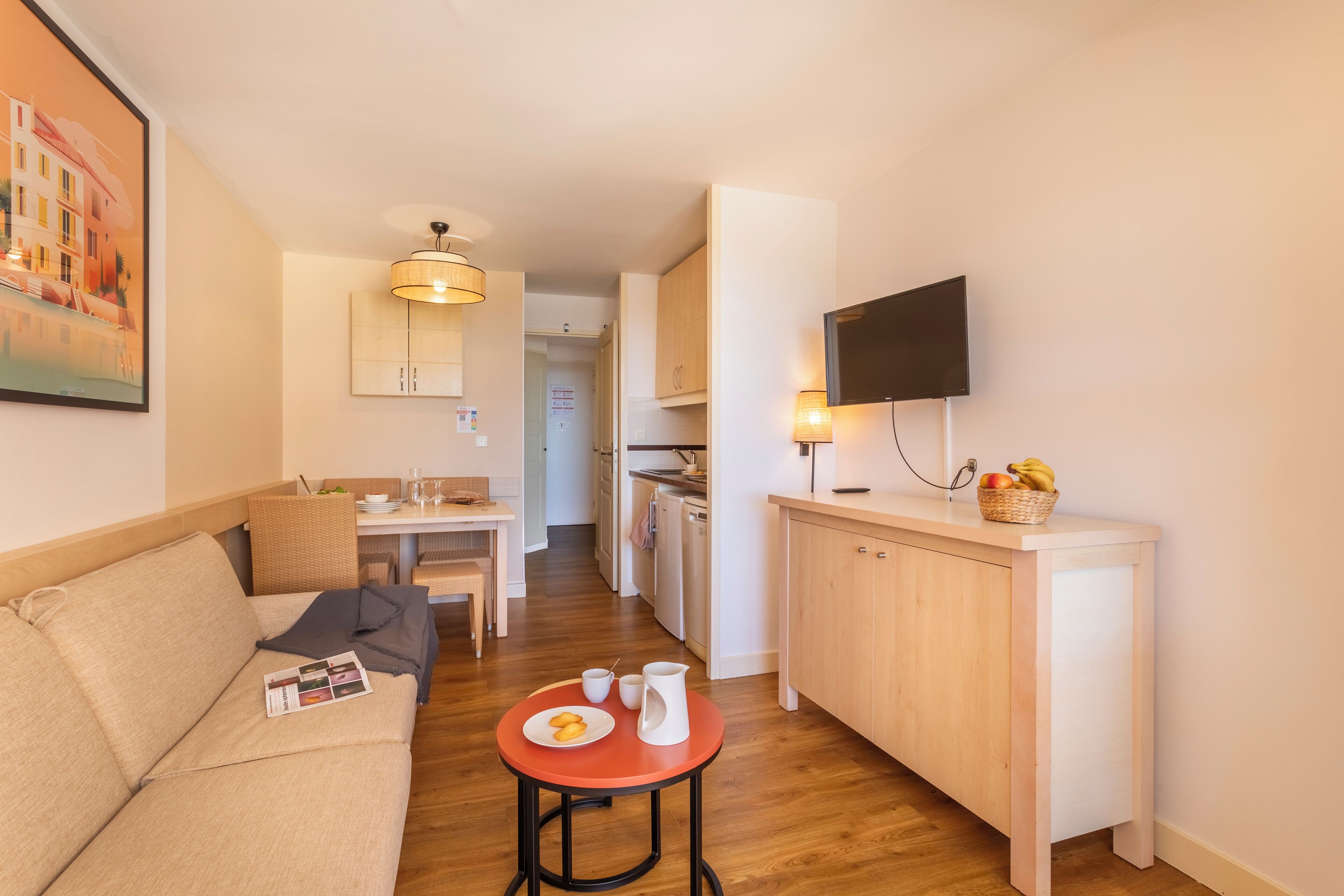 Un espace de vie compact comprenant un canapé, une table à manger, un coin cuisine et un téléviseur fixé au mur.