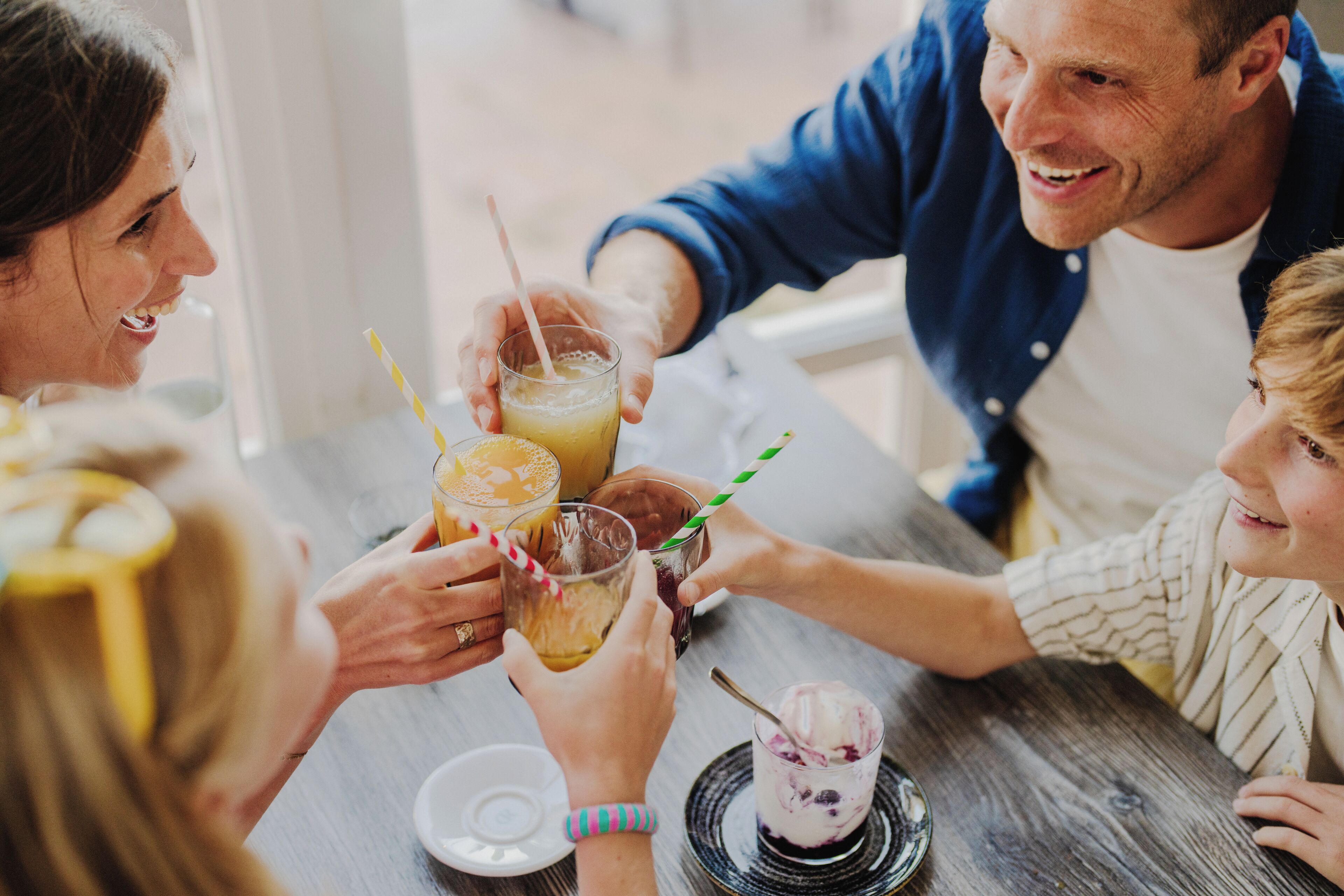 A group of people sitting around a wooden table, holding drinks with straws.