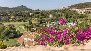 A hotel with a pool, surrounded by lush greenery and a hill in the background.