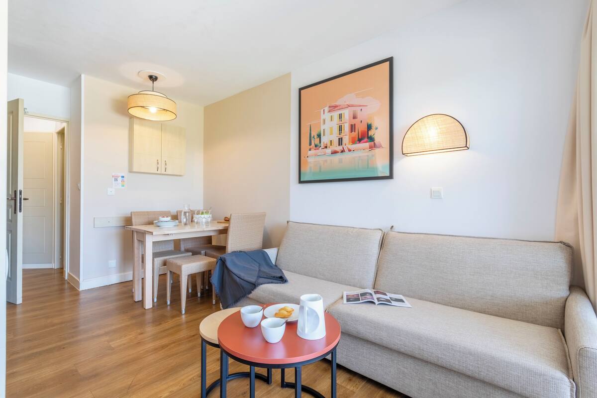 Un salon moderne avec un canapé, une table à manger et des chaises, une petite table basse et un tableau accroché au mur.