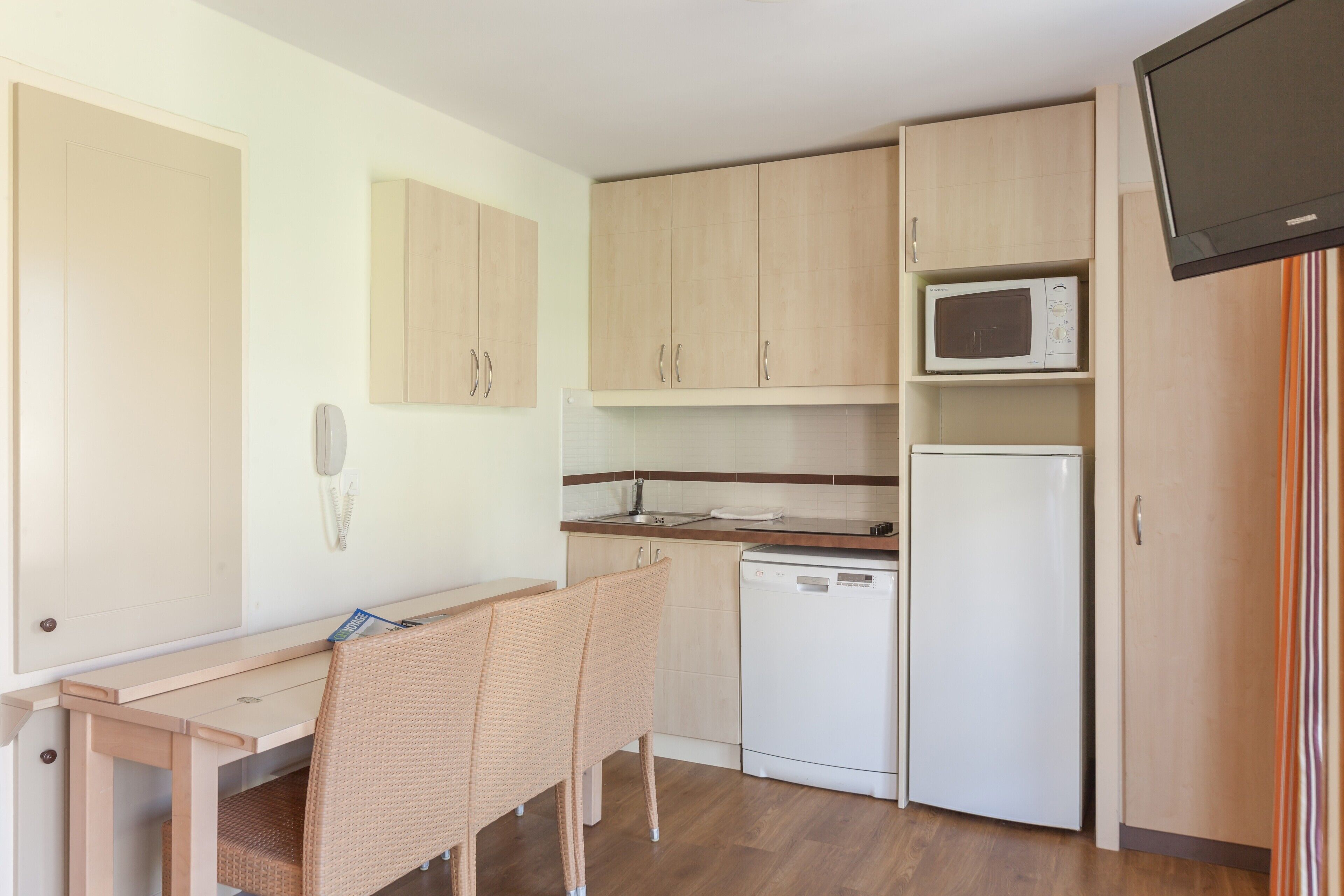 A compact kitchen with a microwave, dishwasher, and a small dining area with a chair.