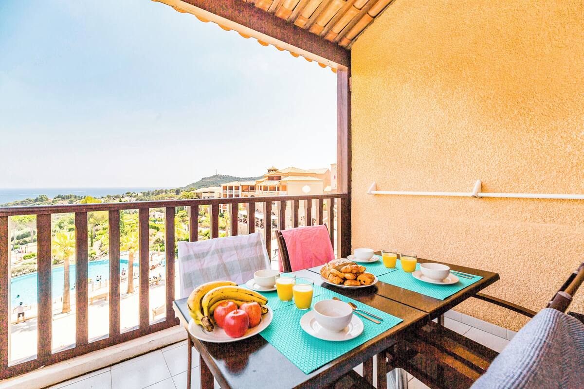 Un balcon avec une table préparée pour le petit-déjeuner, donnant sur une piscine et un paysage montagneux.