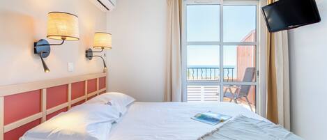 Une chambre d’hôtel comprenant un lit, deux lampes fixées au mur, un climatiseur, une télévision et un balcon avec une chaise.