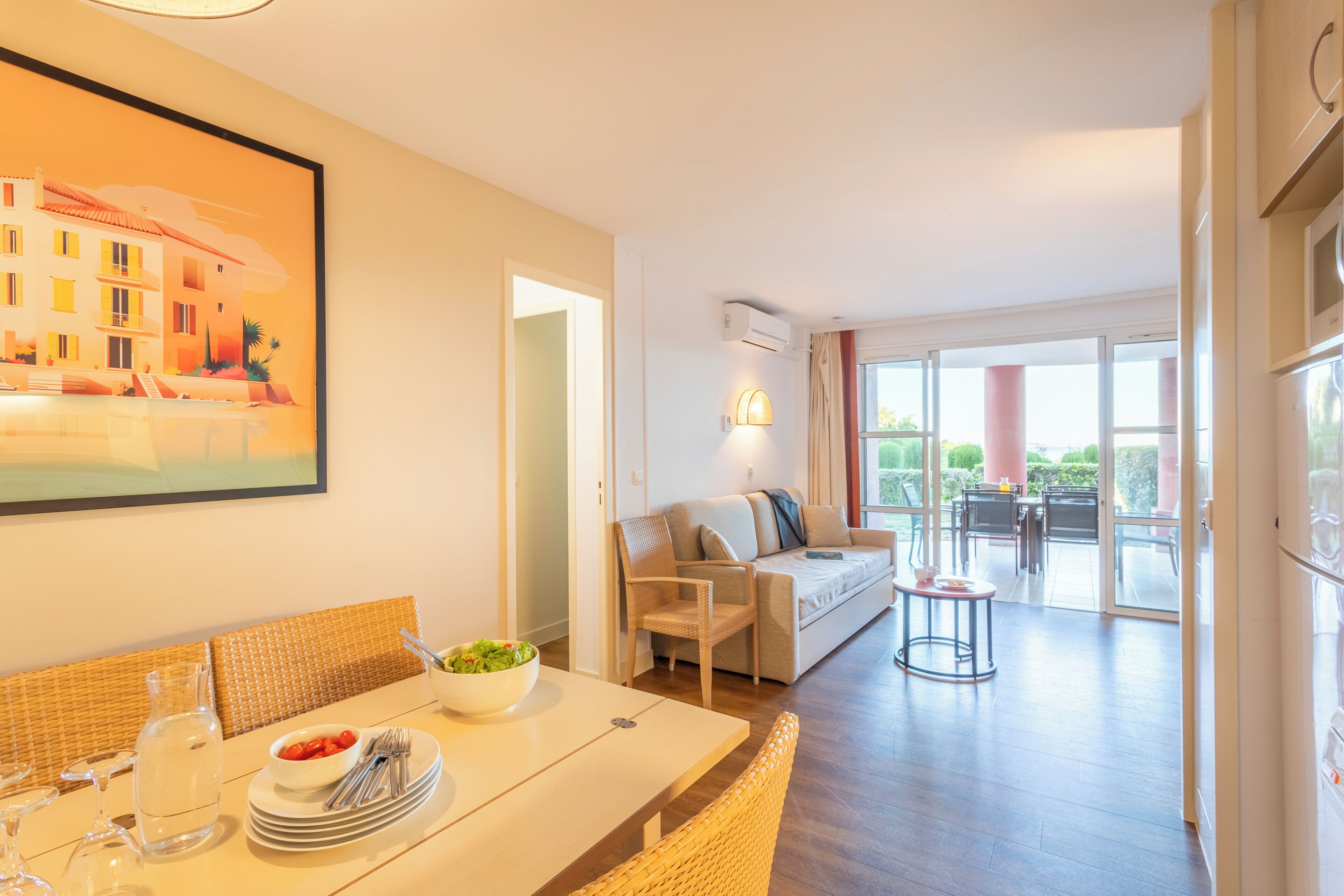 A modern dining area with a table set for two, a sofa, and a balcony with outdoor furniture.