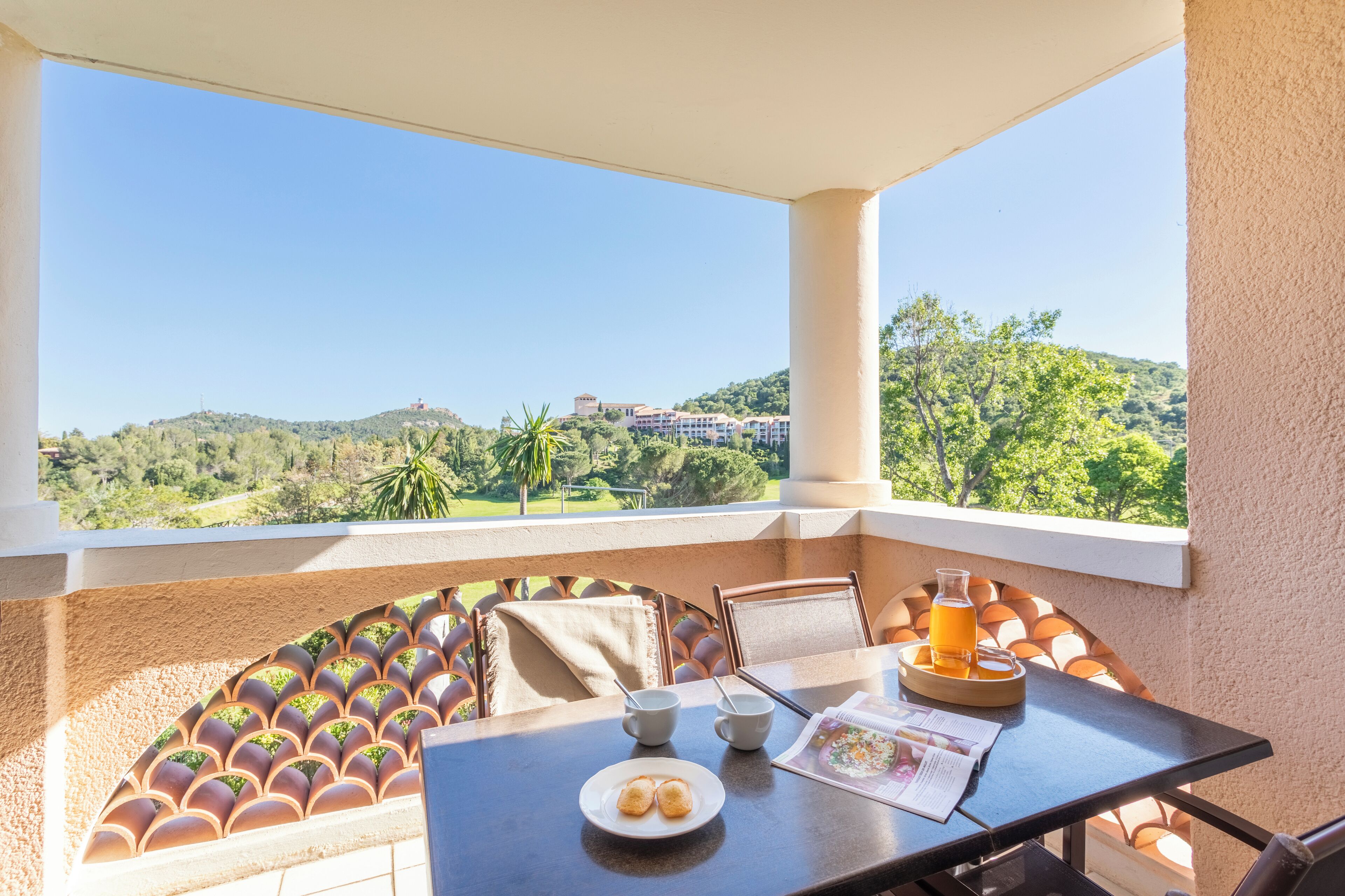 A balcony with a table set for breakfast, including a plate of pastries, a glass of orange juice, and a cup of coffee.