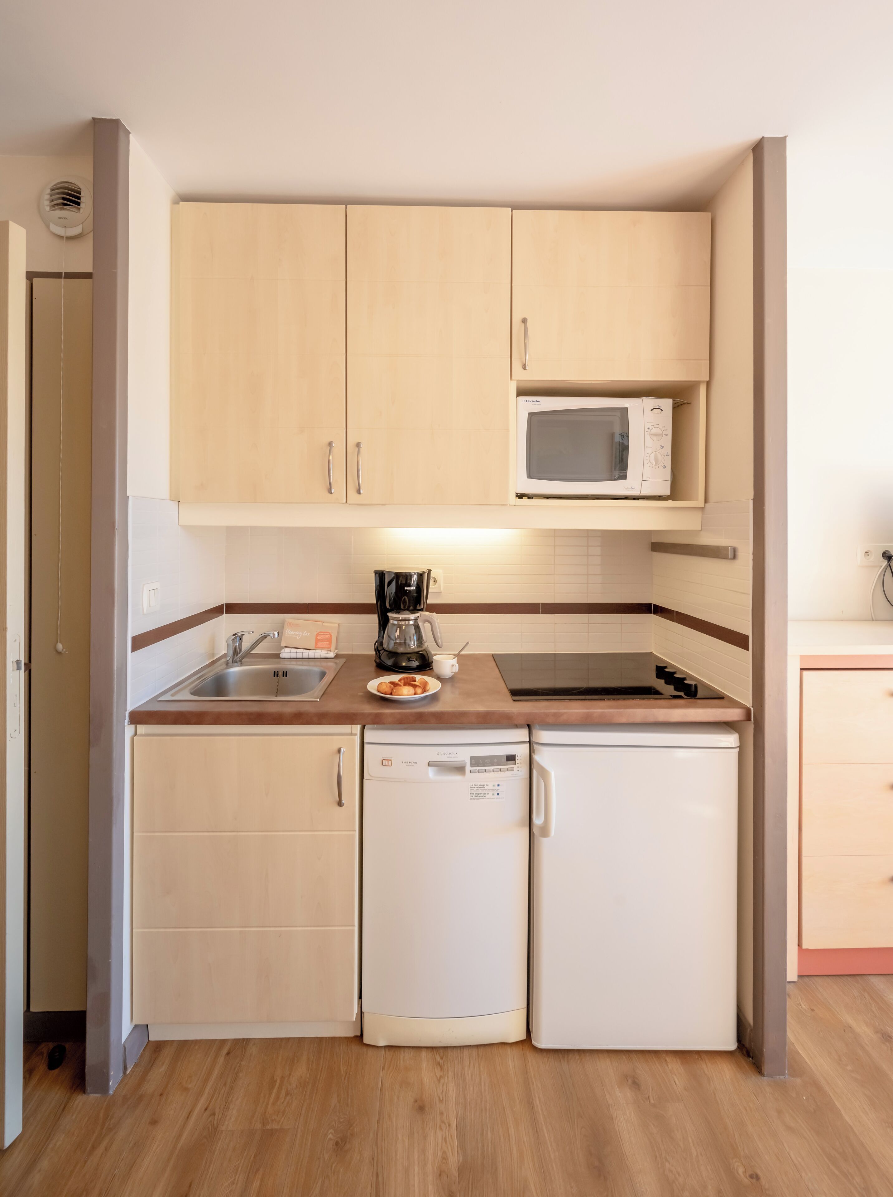 A compact kitchen with wooden cabinets, a microwave, a coffee maker, and a dishwasher.