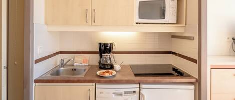 A compact kitchen with wooden cabinets, a microwave, a coffee maker, and a dishwasher.