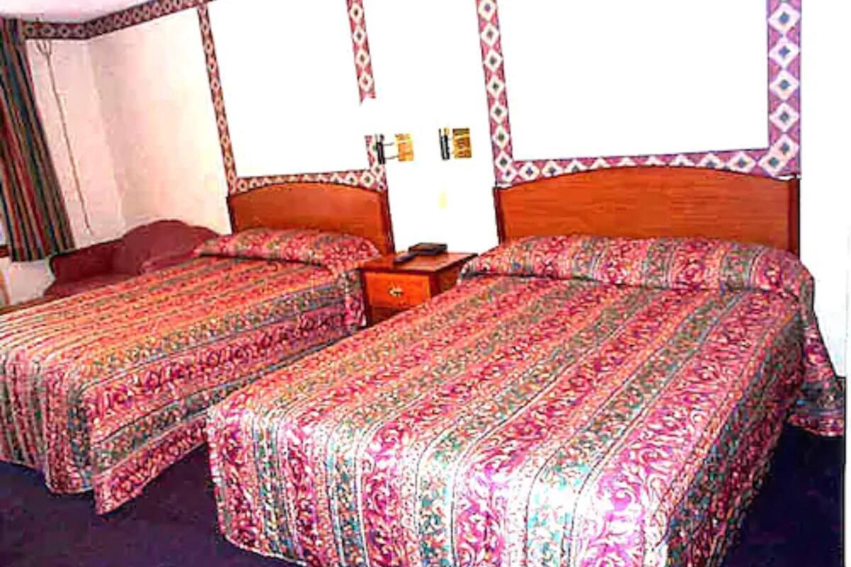 A room with two single beds, a wooden headboard, a nightstand, and a wall with a patterned border.