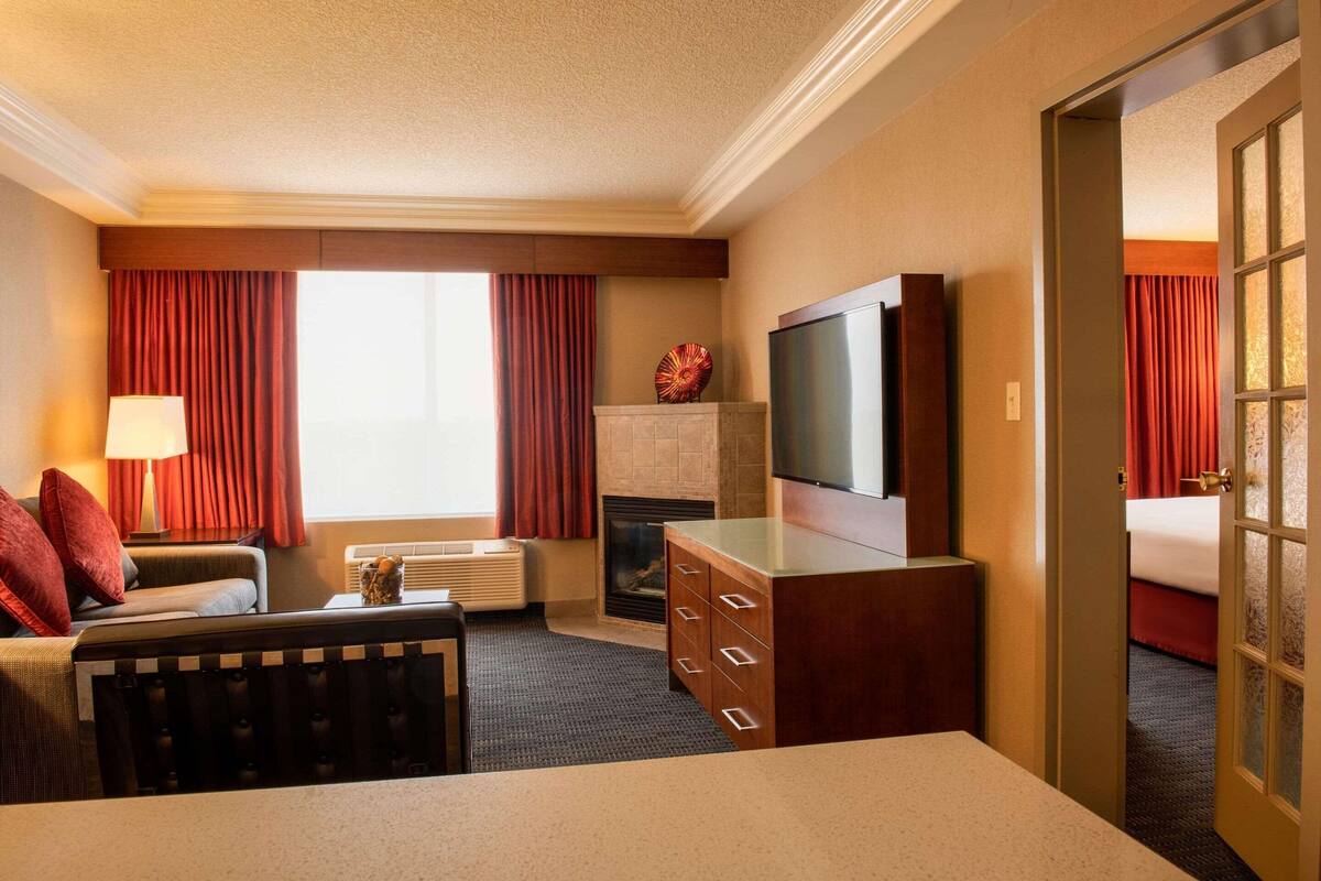 A hotel room with a bed, a TV, a fireplace, a desk, and a window with curtains.