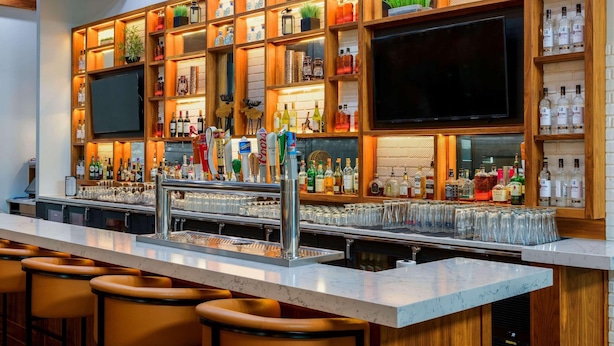 Una zona de bar con una barra alargada, múltiples grifos y una variedad de botellas y vasos.