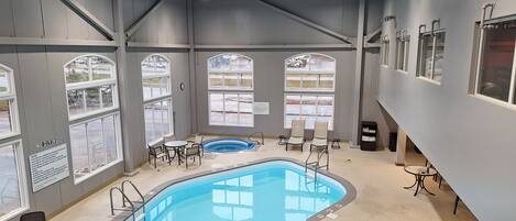An indoor swimming pool with a lounge area, large windows, and a view of the parking lot.