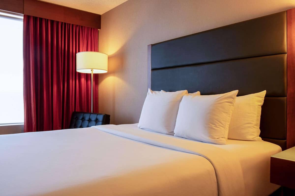 A hotel room with a large bed, a dark headboard, and a red curtain.