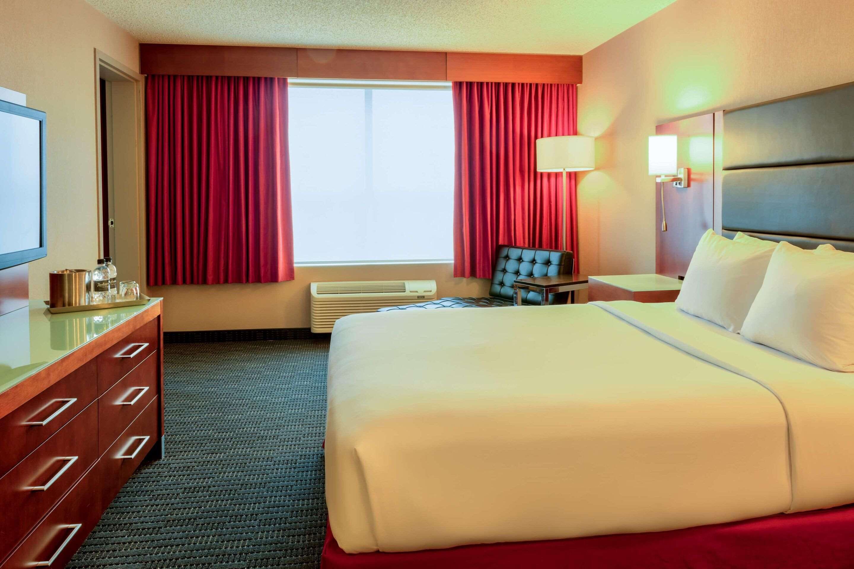 Habitación de hotel con una cama grande, un escritorio, una silla, un televisor y una ventana con cortinas.