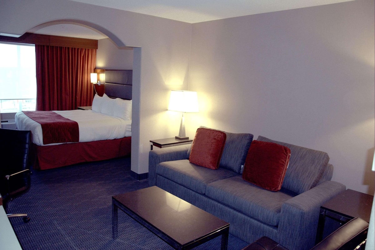 A hotel room with a bed, a sofa, a coffee table, a TV, and a lamp.