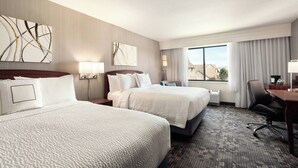 A hotel room with two beds, a desk, a chair, and a large window with curtains.