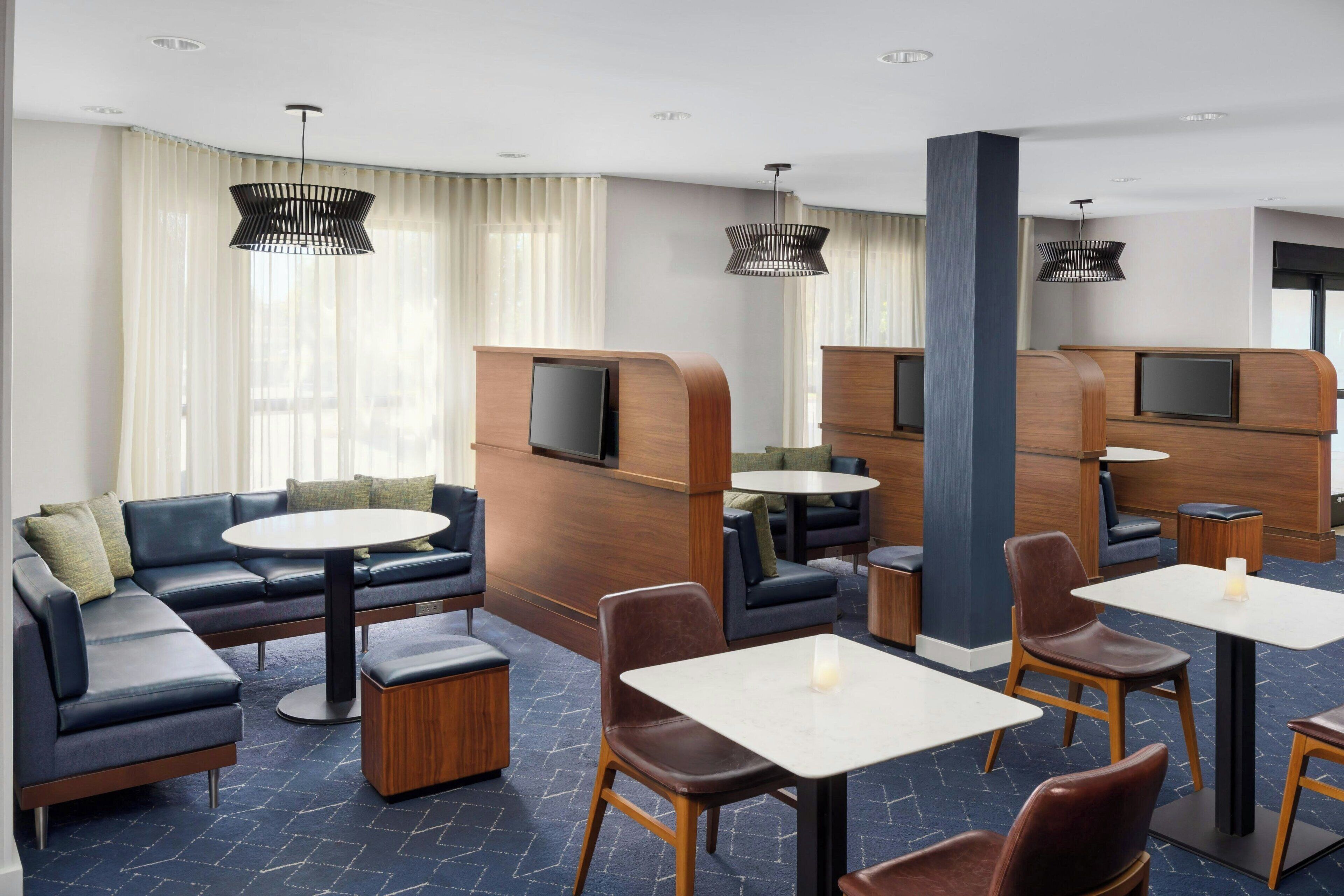 Un moderno vestíbulo de hotel con un sofá modular, mesas redondas y un televisor de pantalla plana montado en un panel de madera.