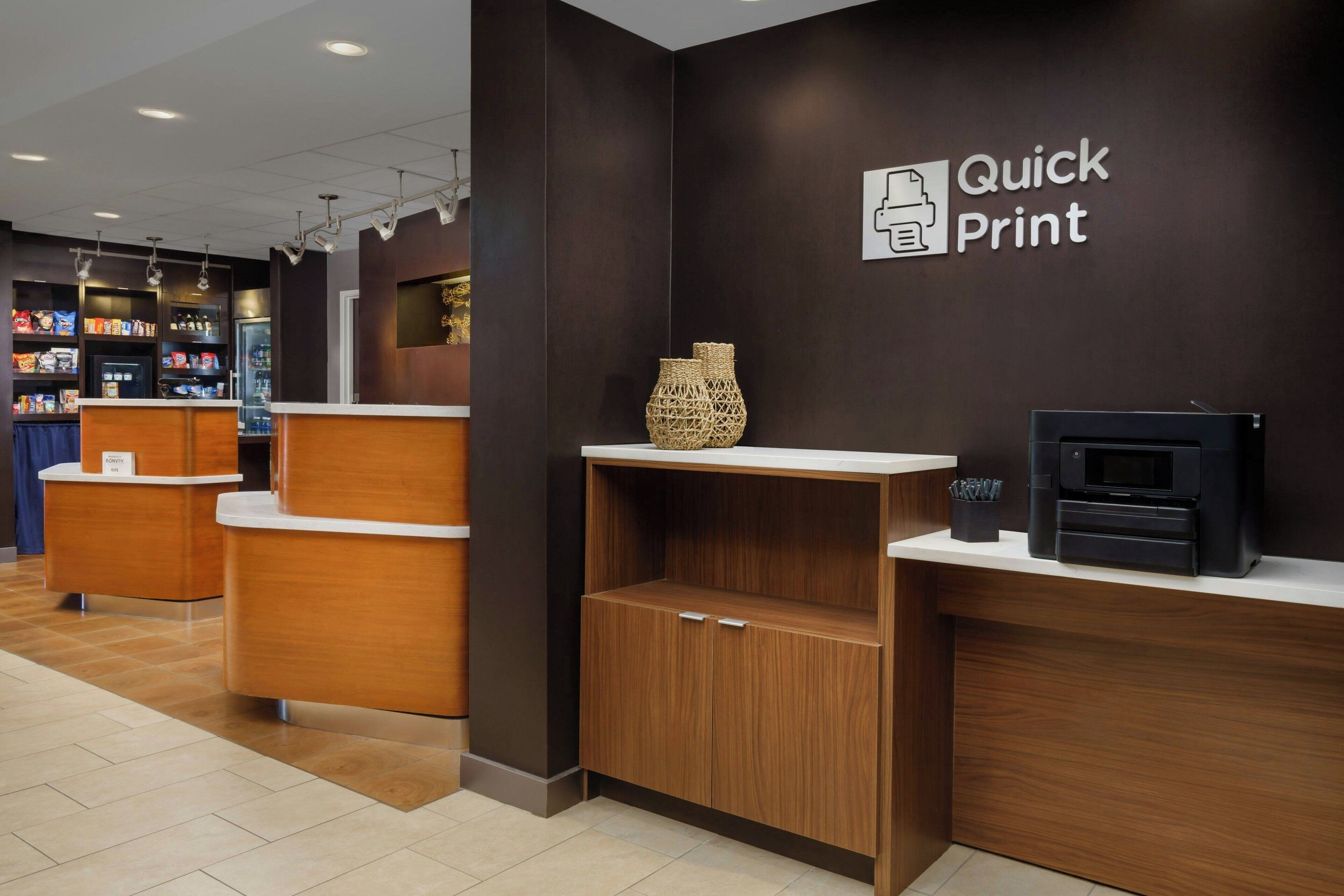 A reception area with a "Quick Print" sign, a printer, and a decorative vase on a shelf.