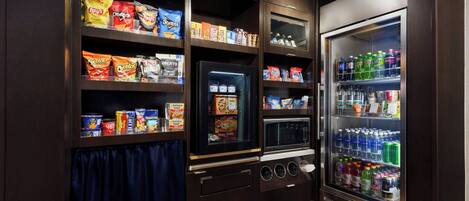 A kitchenette with shelves stocked with snacks and a refrigerator containing beverages.