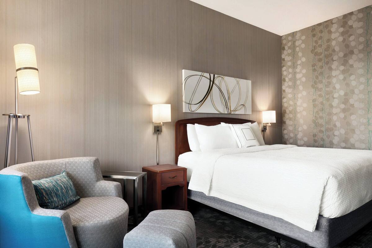 A hotel room with a large bed, a chair, a nightstand, and two wall-mounted lamps.