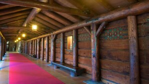 A corridor with wooden walls and a red carpet, featuring a series of benches and a wooden ceiling.