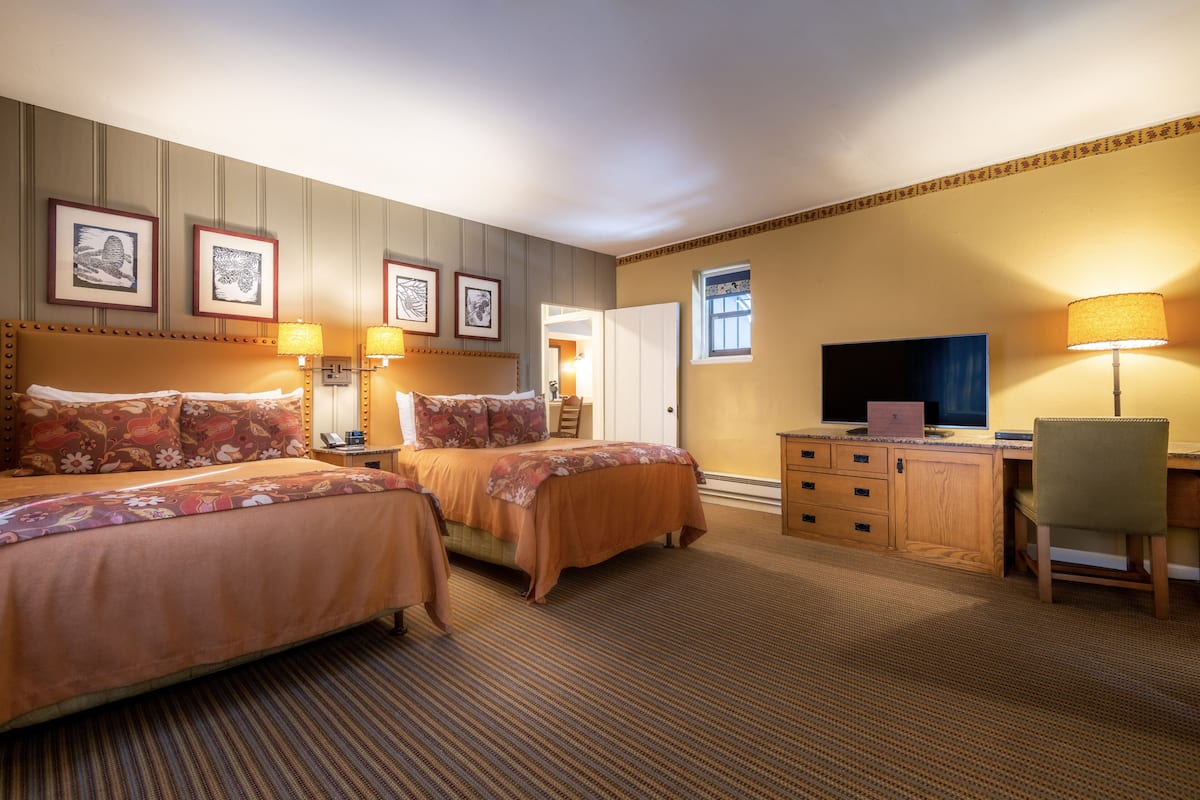Een hotelkamer met twee bedden, een bureau, een stoel, een televisie en lijstjes met kunstwerken aan de muur.